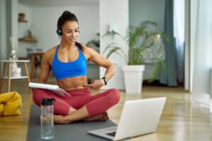 Young fitness instructor using laptop while vlogging about abs exercises at home.