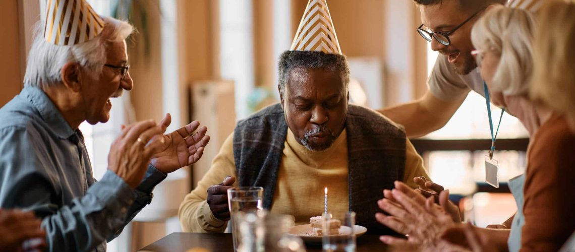 Black senior man blowing Birthday candle on cake in nursing home.
