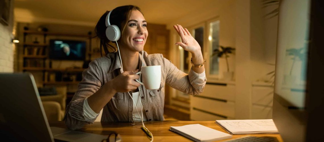 Happy woman with headphones making video call over computer at night.